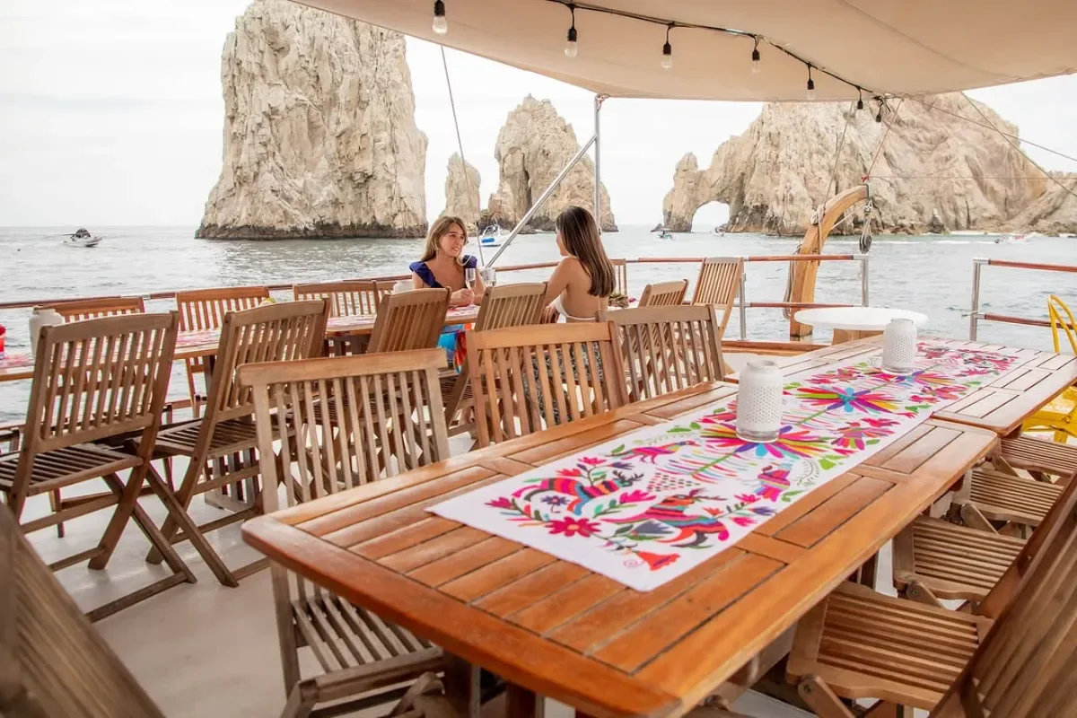 Teak dining table set on deck with the Land's End rocks behind